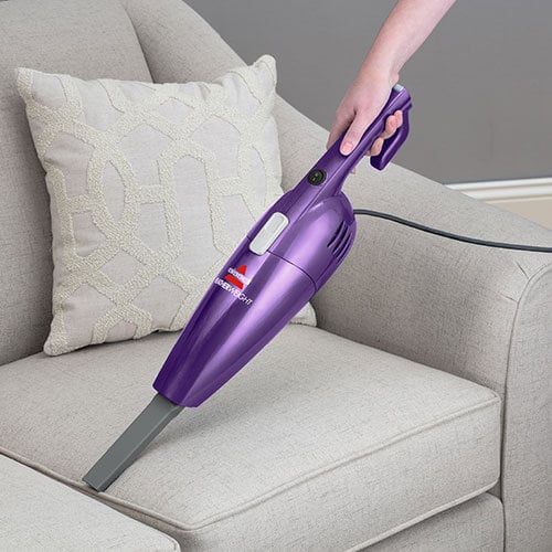 Woman Using FeatherWeight™ Lightweight Stick Vacuum
                        Crevice Tool to Clean Couch