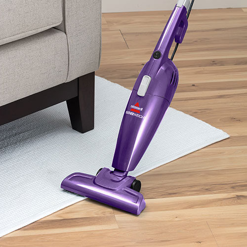 Woman Using FeatherWeight™ Lightweight Stick Vacuum to
                        Clean Area Rug and Hardwood Floors